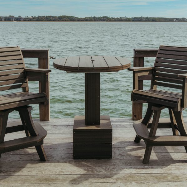 Coastal High Tide Patio Table without an umbrella sits on a dock in Charleston harbor with two High Tide Chairs.
