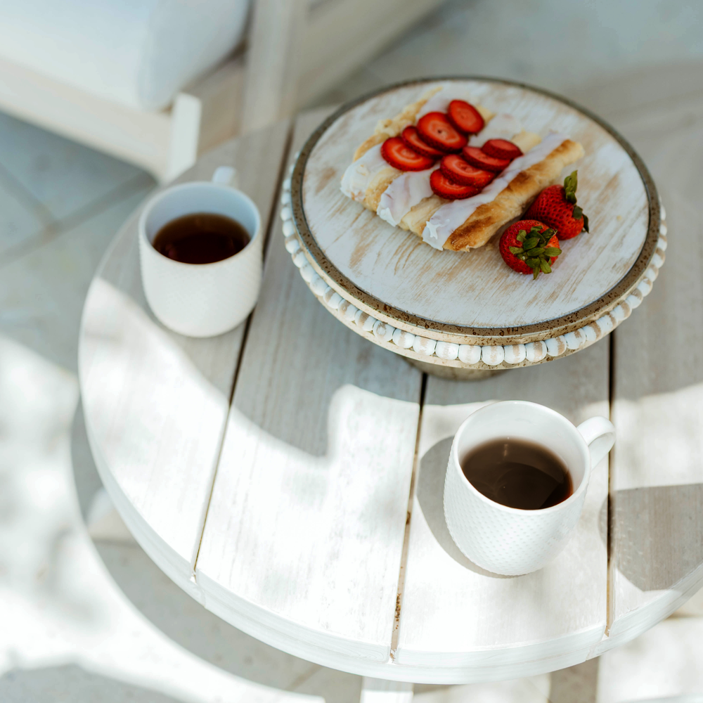 A Seashell Bourbon Outdoor side table and white Bourbon chair, set for coffee and pastries on the patio.