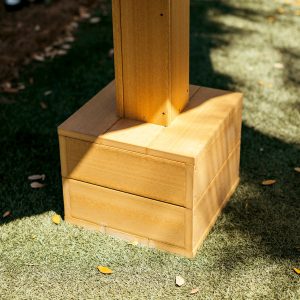 A Teak Box Anchor Outdoor Umbrella Base sits in the sun with a High Tide Table above it. 