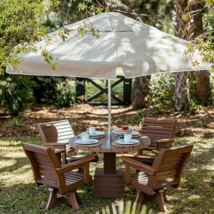 Ebb Tide Outdoor Dining Table Set in Mahogany with a Linen Palmetto umbrella rests on a lawn. 