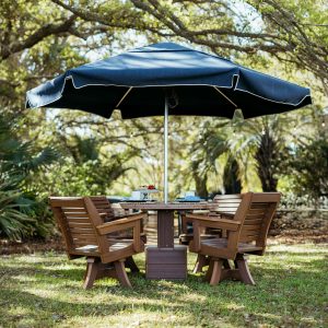 Ebb Tide Outdoor Dining Table Set in Mahogany with a Marine Palmetto umbrella rests on a lawn. 
