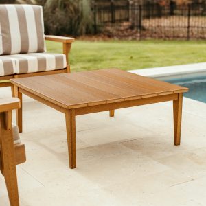 A Mahogany Sweetgrass Outdoor Coffee Table sits near a pool.  