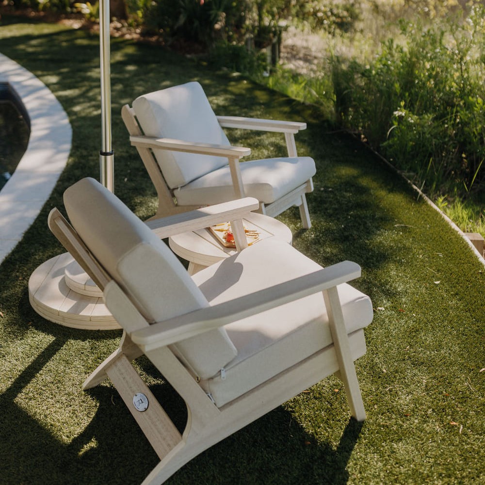 Seashell Bourbon outdoor patio lounge chairs sit on a lawn under an umbrella.
